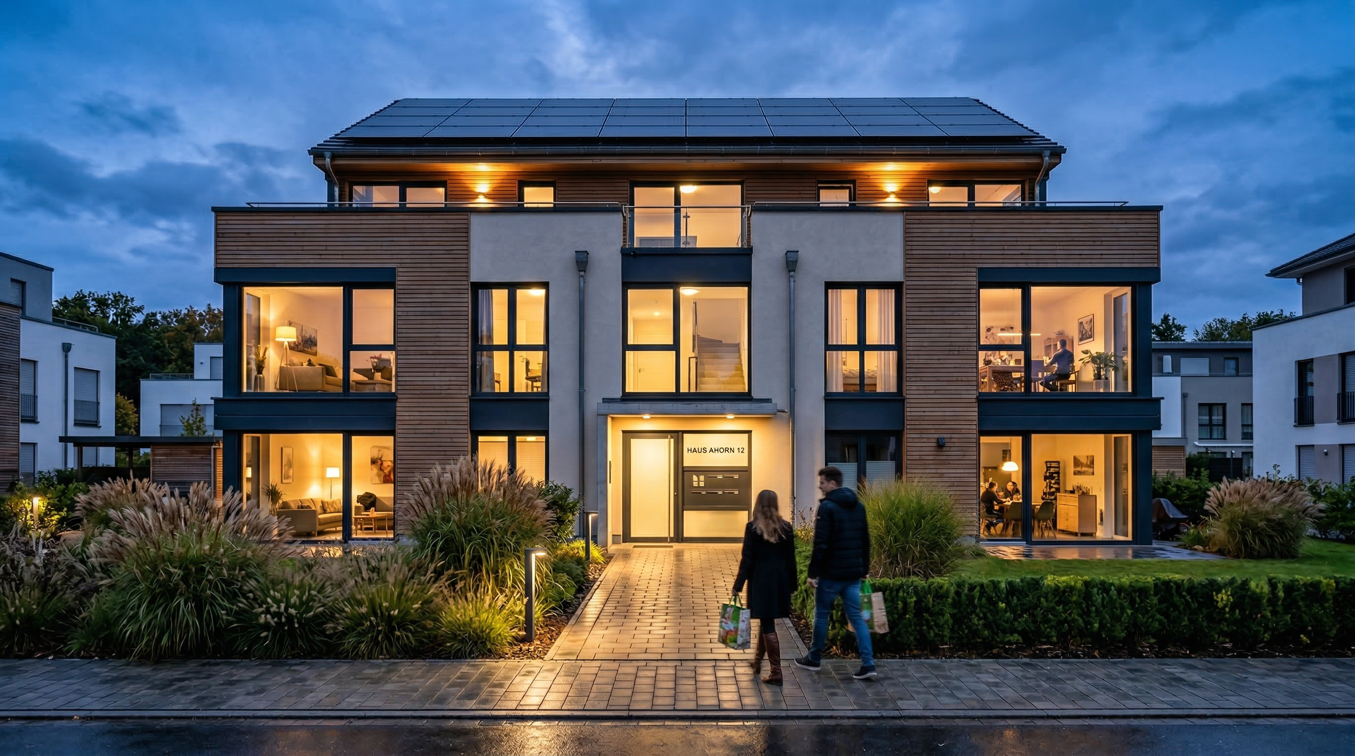 Modernes Mehrfamilienhaus in der blauen Stunde mit warmem Licht und Solaranlage – Neshtec Energieversorgung